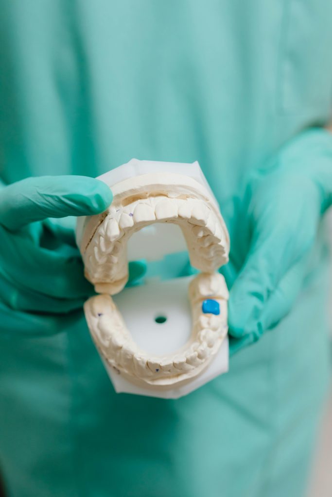 Detailed close-up of gloved hands holding a dental model with white teeth and teal scrubs.